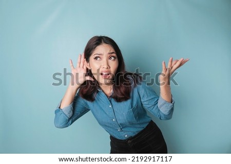 Amazed curious bride young woman wearing a blue shirt trying to hear you overhear listening intently isolated on blue turquoise background studio portrait.