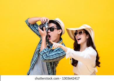 Amazed excited young Asian couple tourists in colorful yellow background