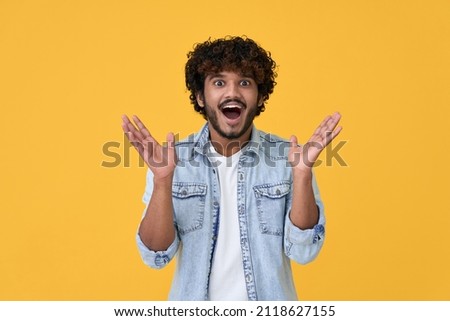 Amazed excited young indian man looking at camera with wow face expression feeling surprised advertising shopping promotion, unbelievable betting win standing isolated on yellow background. Foto d'archivio © 