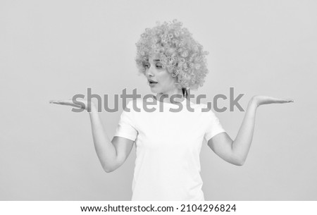 amazed funny girl with fancy look wearing orange hair wig presenting product, copy space, choice.