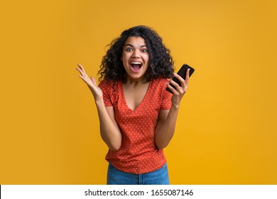 Amazed Girl With Mobile Phone In Hands Celebrating Victory In Online Casino, Hitting Jackpot In Lotttery, Making Bets Online At Bookmaker's Website. Female Blogger Happy To Get One Million Followers. 