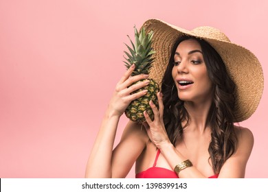 Amazed Girl In Straw Hat And Bikini Holding Pinapple Isolated On Pink