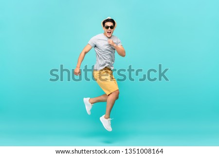 Amazed handsome Asian tourist man jumping studio shot isolated on light blue background