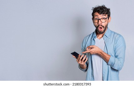 Amazed handsome man pointing at his cell phone isolated, surprised person pointing at his cell phone isolated. Isolated teenager surprised of a promotion on his cell phone