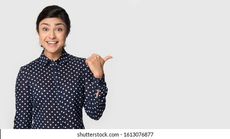 Amazed happy indian young girl raising eyebrows in astonishment, standing on left, pointing aside on empty blank free copy space for advertisement text, good deal big discount shopping opportunity.
