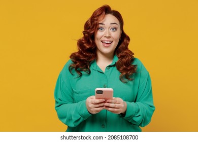 Amazed Happy Vivid Young Ginger Chubby Overweight Woman 20s Wears Green Shirt Hold In Hand Use Mobile Cell Phone Texting Typing Reading Searching Isolated On Plain Yellow Background Studio Portrait