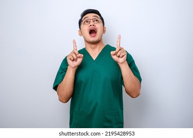 Amazed And Impressed Asian Male Nurse, Doctor In Scrubs Pointing Fingers Up And Looking Questioned, Interested In New Promo, White Background