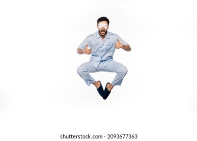 Amazed Man In Blue Pajamas And Sleeping Mask Levitating While Showing Thumbs Up On White