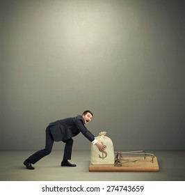 Amazed Man In Formal Wear Reaching His Hands To Take Bag With Money In Big Mousetrap Over Dark Grey Background With Empty Copyspace Overhead