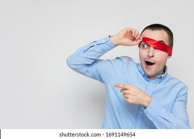 Amazed Man Removes Red Blindfold And Points To Copy Space, Portrait, White Background