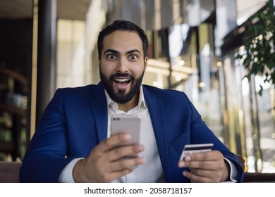 Amazed middle eastern businessman holding mobile phone shopping online. Sales, black Friday concept. Happy successful Arabic man receive payment Amazed middle eastern businessman holding mobile phone shopping online. Sales, black Friday concept. Happy successful Arabic man receive payment