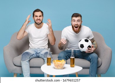 Amazed nervous men guys friends in white t-shirt sit on couch isolated on pastel blue background. Sport leisure lifestyle concept. Cheer up support favorite team with soccer ball doing winner gesture - Shutterstock ID 1679651257