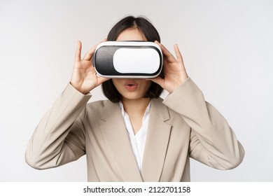 Amazed office woman, asian business person in suit, wearing vr headset, looking at smth in virtual reality glasses with impressed, wow face, white background - Powered by Shutterstock