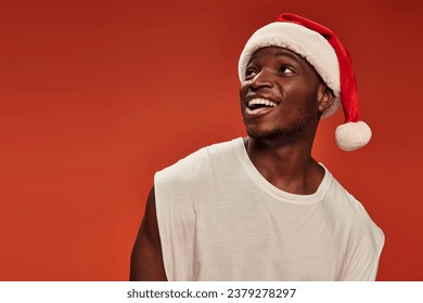 amazed and overjoyed african american man in santa cap smiling and looking away on red backdrop - Powered by Shutterstock