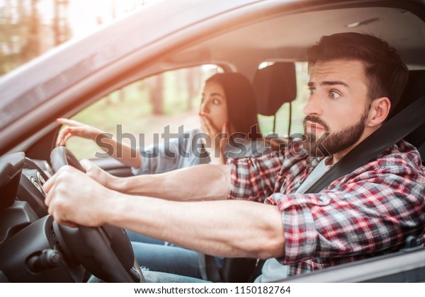 Amazed people are sitting in car
and looking straight forward. They are frustrated. Girl is covering
her mouth with one hand and pointing forward with another
one