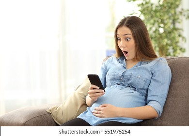 Amazed pregnant woman watching media content in a smart phone sitting on a sofa in the living room in a house interior - Powered by Shutterstock