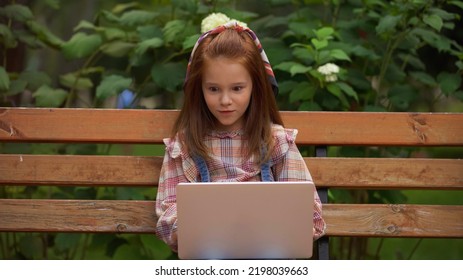 Amazed Redhead Kid Using Laptop On Bench In Park