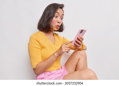 Amazed surprised Asian woman stares at smartphone received bank debt notification reads sms with unbelievable news makes big eyes excited by online lottery win job promotion or great shopping offer