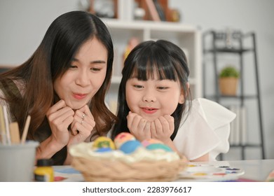 Amazed and surprised young Asian girl enjoys making Easter eggs with her sister in the kitchen. - Shutterstock ID 2283976617