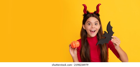 amazed teen girl wearing imp horns holding pumpkin and bat on yellow background. Halloween kid girl portrait, horizontal poster. Banner header with copy space. - Shutterstock ID 2198234979