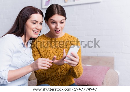 amazed teenage girl looking at smartphone near mother