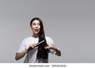 Amazed Woman Using Hair Straightener Isolated On Grey