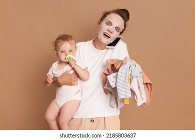 Amazed woman wearing white t shirt doing cosmetic procedures, holding baby daughter in hands and kid's clothing, talking via cell phone with her friend, isolated over brown background. - Powered by Shutterstock