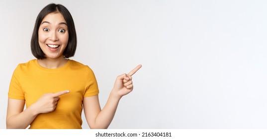 Amazed Young Asian Woman, Showing Advertisement Aside, Pointing Fingers Right At Promotion Text, Brand Logo, Standing Happy Against White Background