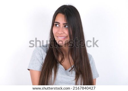 Amazed young caucasian woman wearing grey t-shirt over white background bitting lip and looking tricky to empty space.