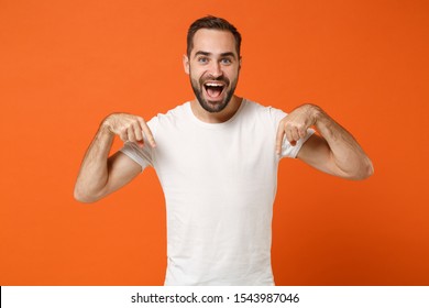 Amazed Young Man In Casual White T-shirt Posing Isolated On Bright Orange Wall Background Studio Portrait. People Sincere Emotions Lifestyle Concept. Mock Up Copy Space. Pointing Index Fingers Down