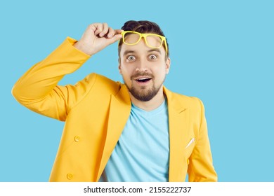 Amazed young man isolated on blue studio background take of glasses shocked by unbelievable news. Stunned male surprised by amazing sale deal or promotion offer. Advertising and commerce.