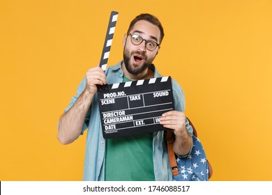 Amazed Young Man Student In Casual Clothes Glasses With Backpack Isolated On Yellow Wall Background. Education In High School University College Concept. Hold Classic Black Film Making Clapperboard