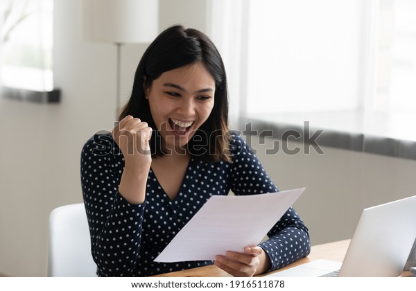 Amazed young mixed race female student hold\
official written letter with good test exam results. Happy asian\
woman look at paper document celebrate admission to university\
receive grant\
scholarship