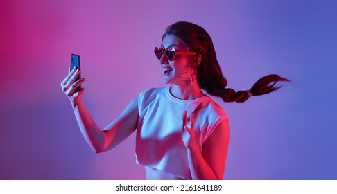 Amazed Young Woman Using Mobile Phone Isolated On Neon Background. Digital Media Technology 5g Concept.