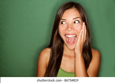 amazement - woman excited looking to the side. Surprised happy young woman looking sideways in excitement. Mixed race Chinese Asian / white Caucasian female model on green background.