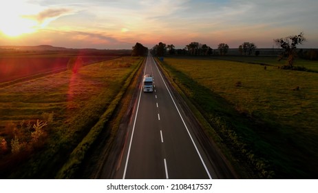 Amazing Aerial Drone View: White Lorry Delivering Goods by Road. Sunset Summer time: Blue Sky, Red Sun. Sun Rays Shining the road.