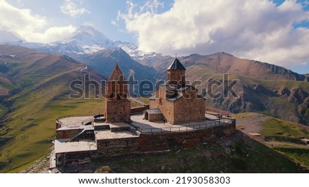 amazing aerial view of Gergeti Trinity Church surrounded by the Caucasus mountains in the sunny weather, Kazbegi, Georgia. High quality photo