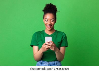 Aplicação incrível. Retrato de mulher negra feliz usando smartphone na parede verde do estúdio Foto Stock