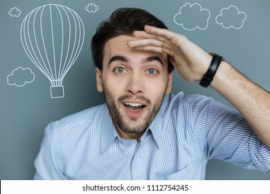 Amazing balloons. Emotional positive young man putting his eyebrows up and looking excited while watching amazing hot air balloons flying - Shutterstock ID 1112754245