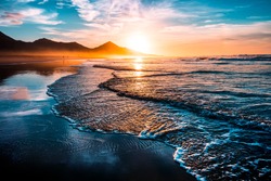 Amazing Beach Sunset With Endless Horizon And Lonely Figures In The Distance, And Incredible Foamy Waves. Volcanic Hills In The Background.