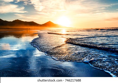 Erstaunlicher Sonnenuntergang am Strand mit endlosem Horizont und einsamen Figuren in der Ferne
