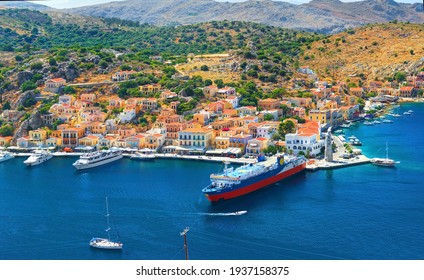 Amazing Beautiful View On Greek Houses On Symi Greece Island Hills With Houses And Trees, Yachts At Sea Port, Tourist Ferryboat At Aegean Sea Bay. Greece Islands Holiday Vacation Cruise And Tours