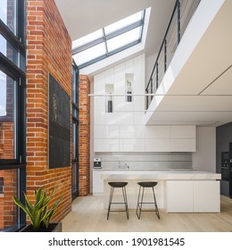 Amazing big windows in loft style apartment with white, spacious and luxury kitchen, exposed red bricks on the walls and mezzanine