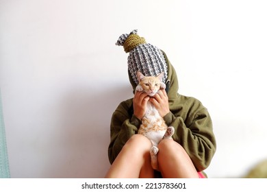 Amazing Concept With Woman That Head Cover By Kitting Scarf, People Head Look Like Pineapple, Hold Cat In Hand With Old Big Book, Sitting With White Wall Background Make Funny Scene