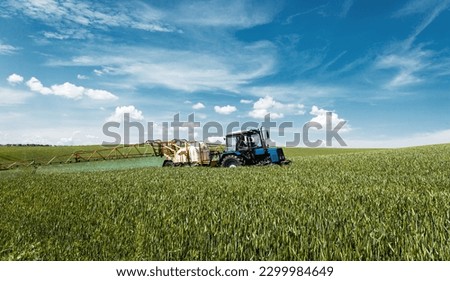 Amazing counryside with green wheat field and  blue sky. Tractor spraying pesticides on wheat field with sprayer sunny day. Wonderful rural landscape. Agricultural and rich harvest concept. 