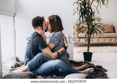 Amazing couple sitting on the rug near the window and kiss one another. Love story, family, spouses