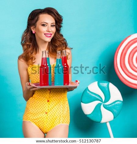 Amazing cute young pretty girl on the turquoise background holding a tray with soda bottles in bright, dressed in a yellow body dresses, perfect makeup and hairstyle, cool, fashion, smiling, fast food