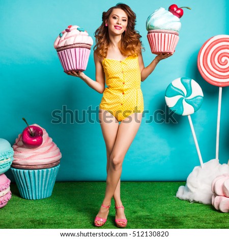 Amazing cute young pretty girl on the turquoise background holding a Huge sweets, Cake, candy, bright yellow body dresses, perfect makeup and hairstyle, fashionable Pin up girl, cool, smiling