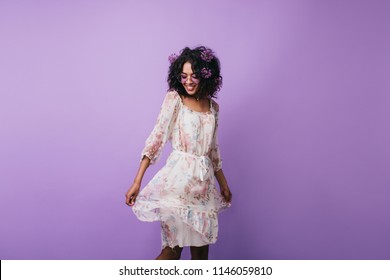 Amazing Dark-haired Girl Posing In Trendy Summer Dress In Studio. Portrait Of Gorgeous African Woman Dancing With Inspired Smile On Purple Background.