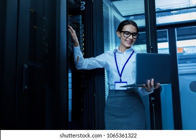 Amazing day. Happy beautiful woman working in a server cabinet and holding her laptop